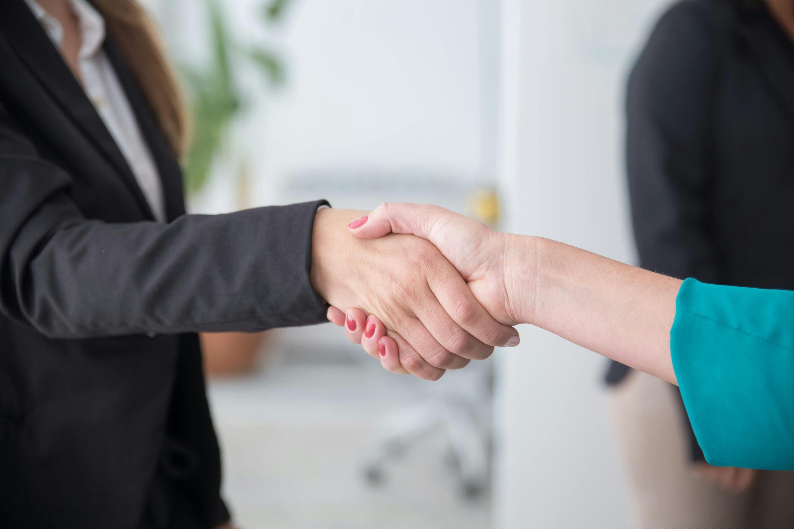 Close-up of a professional handshake between businesswomen in an office environment.